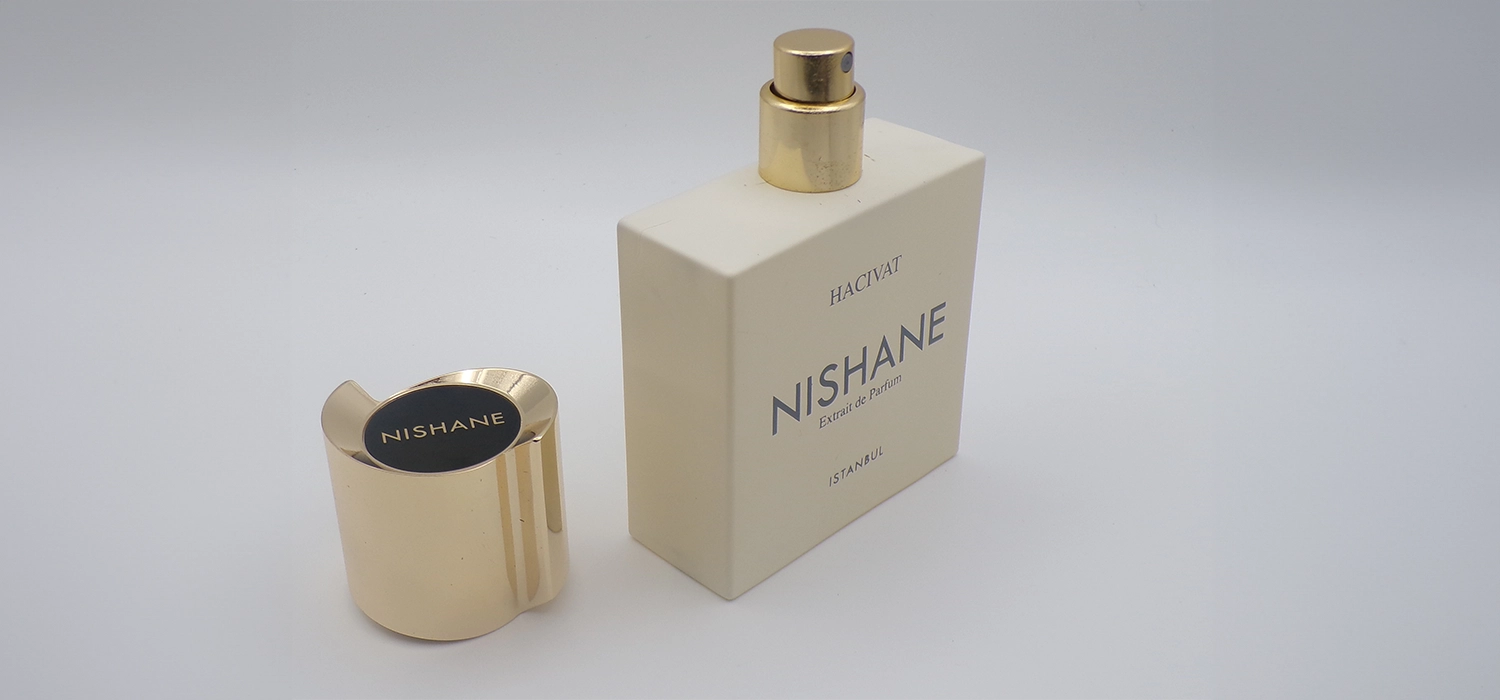 A bottle of perfume next to a gold cap.